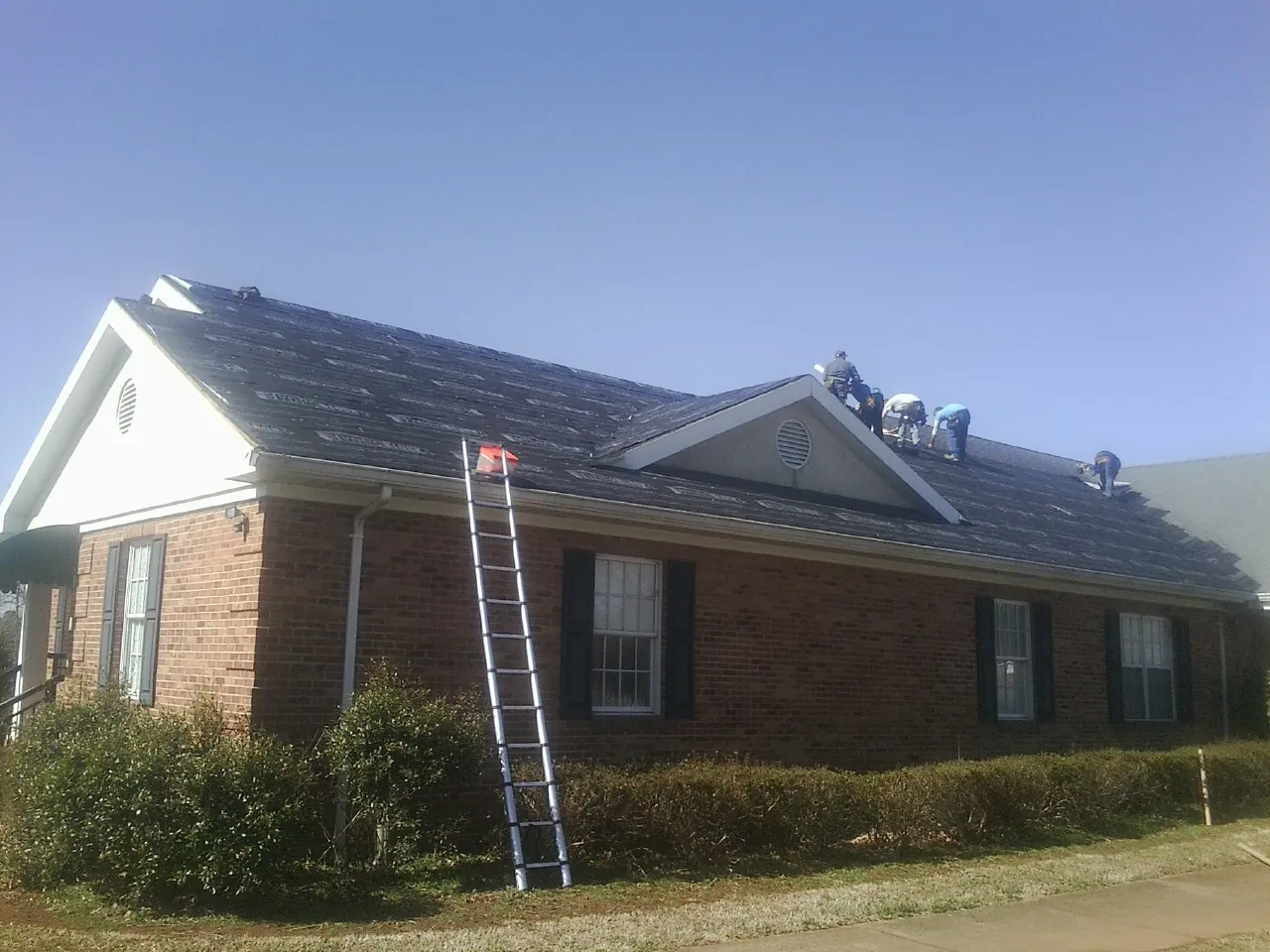 Crew tearing shingles off a brick ranch roof with a ladder set — Metal Roof Repair work by our crew in Chiefland