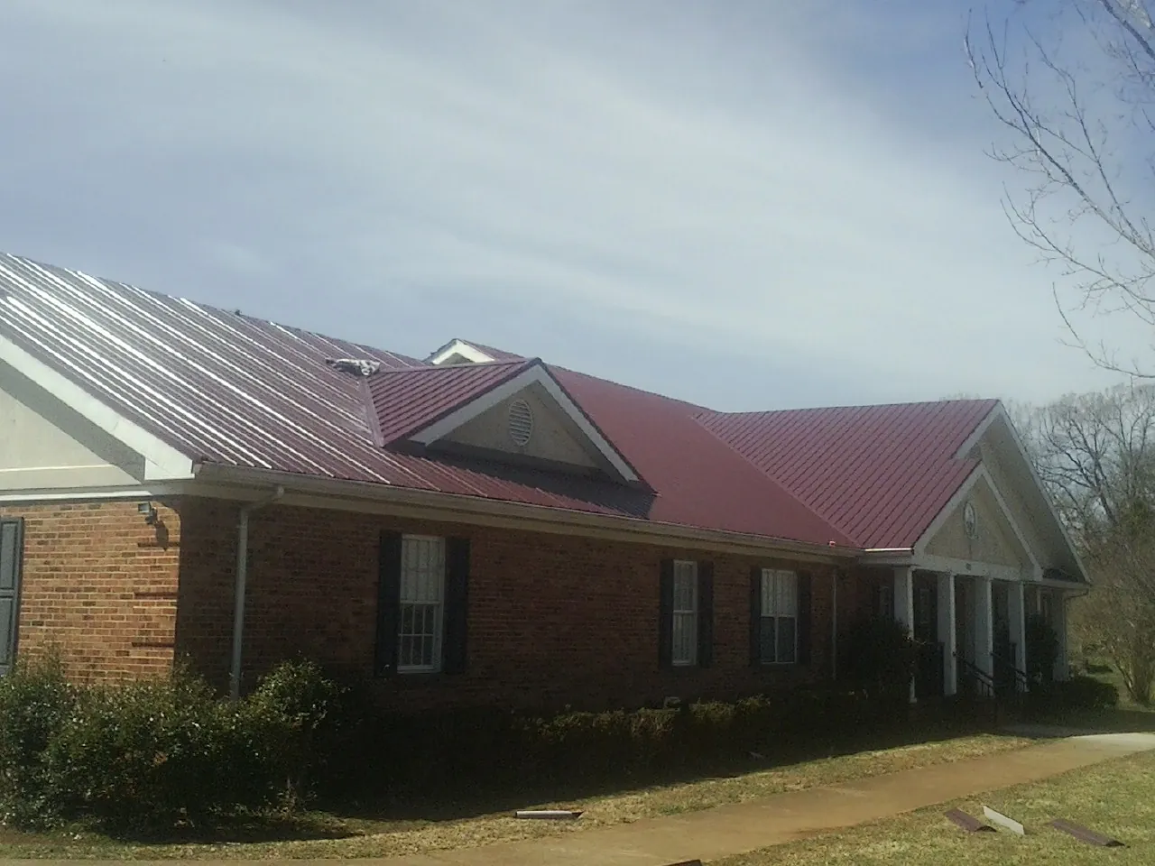 Red metal roof with gabled entries on a long brick building, from a Hail Damage Roof Repair job in Chiefland