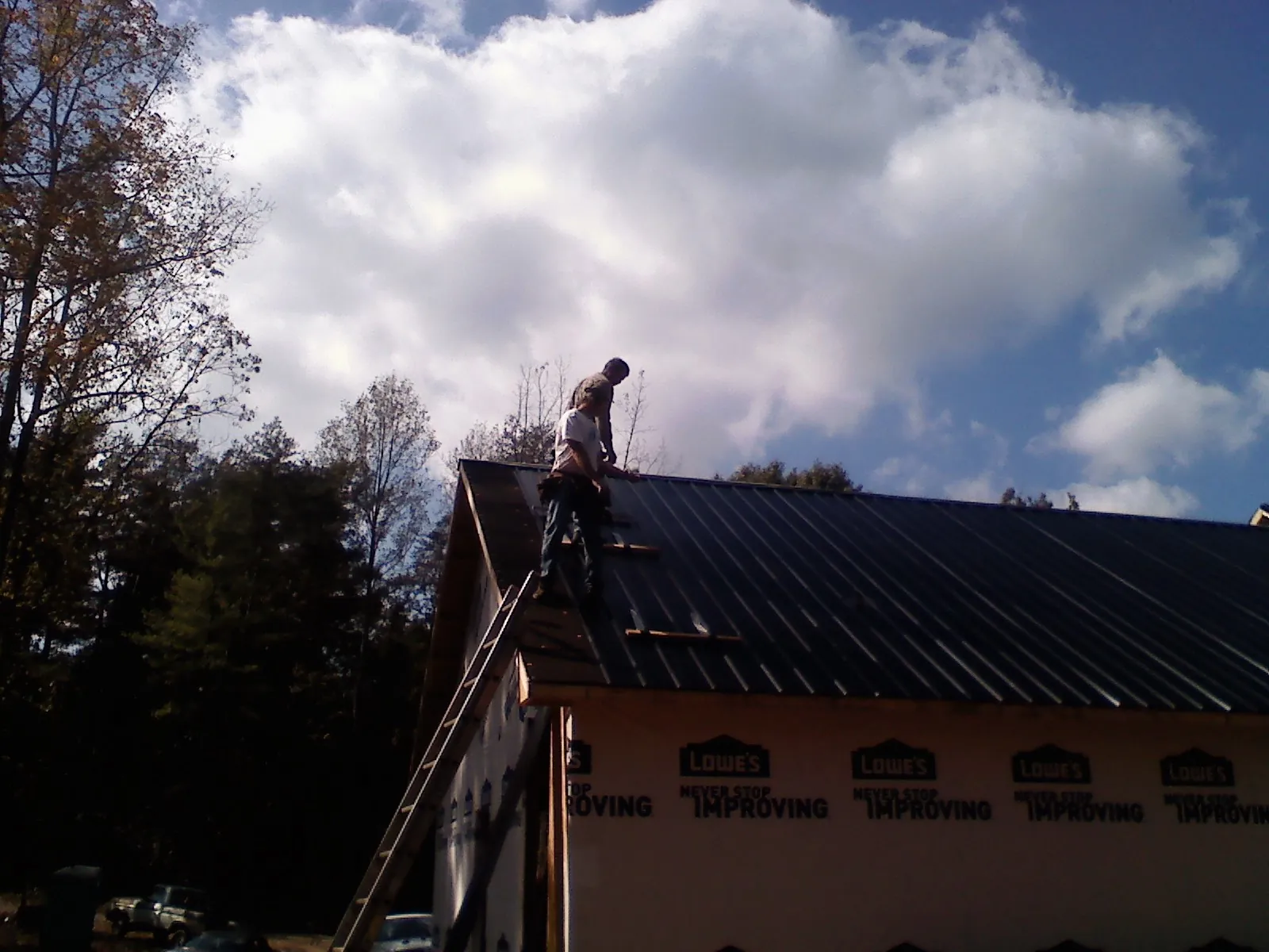 Roofer fastening dark metal panels high against a cloudy sky, from a Roof Inspection job in Chiefland