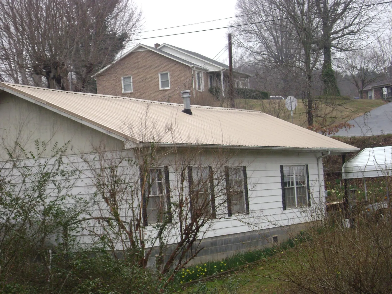 Tan metal roof on a white sided house set into a hillside — Commercial Roofing by Roofing Brothers in Chiefland